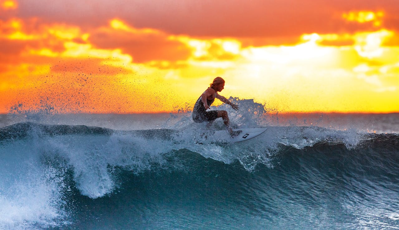 hero-img Surfer riding a wave during a stunning sunset, capturing the thrill of water sports.